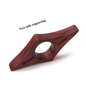 May include: A dark brown wooden bookmark with the words "Alexandre" and "Jennifer" engraved on each side. The bookmark is shaped like a diamond with a hole in the center.