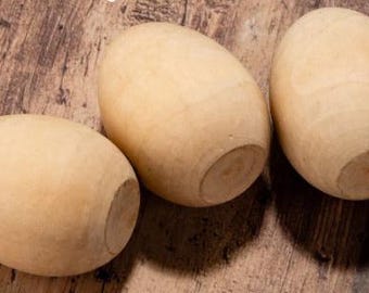 May include: Three wooden eggs, painted a light brown color, are arranged in a row on a wooden surface.