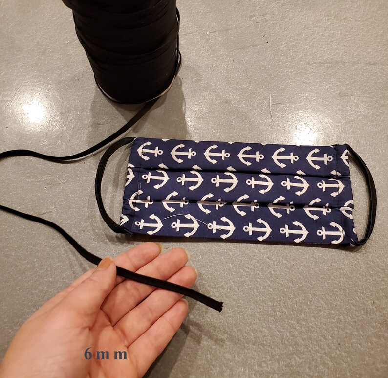 May include: A blue face mask with a white anchor pattern. The mask has black elastic ear loops that are 6 mm wide.