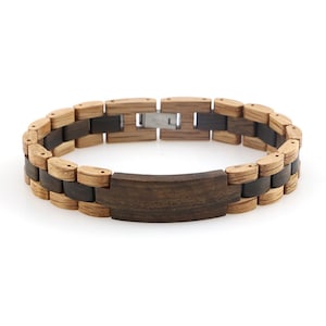 Puede incluir: Un brazalete de madera con una incrustación de madera marrón oscuro y un cierre plateado. El brazalete está hecho de dos tipos diferentes de madera, una clara y otra oscura.