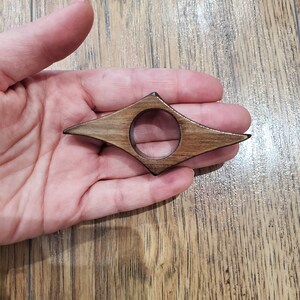 May include: A wooden bookmark shaped like a diamond with a hole in the center. The bookmark is brown with darker wood grain.