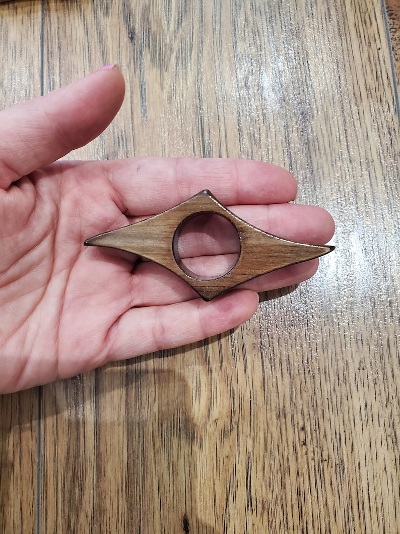 May include: A wooden bookmark shaped like a diamond with a hole in the center. The bookmark is brown with darker wood grain.