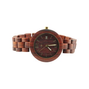 May include: A wooden wristwatch with a brown wooden band and a round, dark red face. The watch face has gold-colored hands and hour markers.