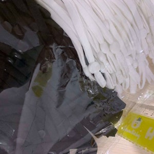 May include: A close-up of a bundle of white elastic cords with white plastic tips. The cords are packaged in a clear plastic bag and are lying on a wooden surface.