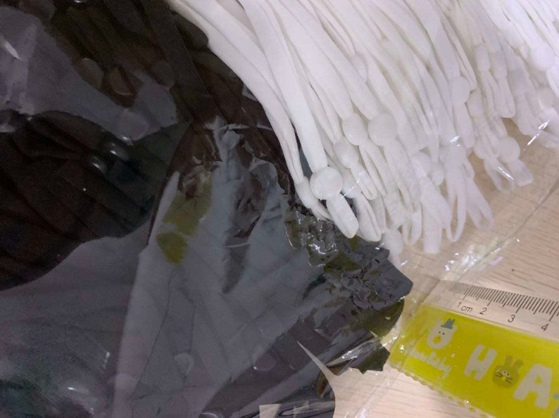 May include: A close-up of a bundle of white elastic cords with white plastic tips. The cords are packaged in a clear plastic bag and are lying on a wooden surface.