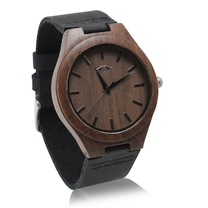 May include: A brown wooden wristwatch with a black leather band. The watch face has black hands and black hour markers.