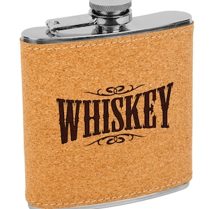 May include: A stainless steel flask with a cork exterior. The flask has a silver cap and hinge. The word "WHISKEY" is printed in dark brown, stylized lettering on the front of the flask.