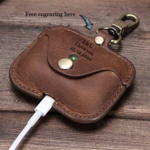 May include: Brown leather Airpods case with a keychain and a personalized engraving that reads "J&L I love you 25.12.2020".