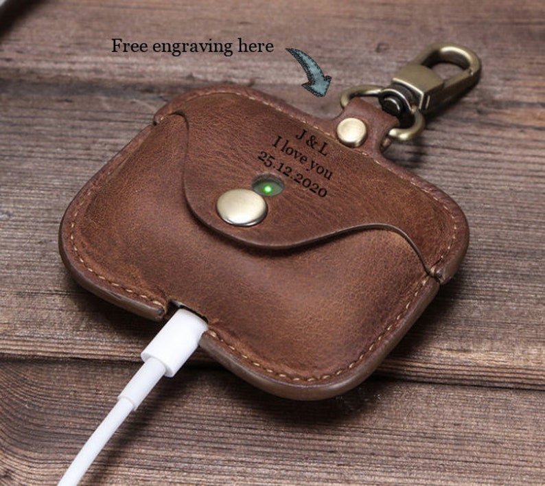 May include: Brown leather Airpods case with a keychain and a personalized engraving that reads "J&L I love you 25.12.2020".