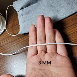 May include: White elastic cord measuring 3 mm in diameter. The cord is held in a hand, with the measurement written below.