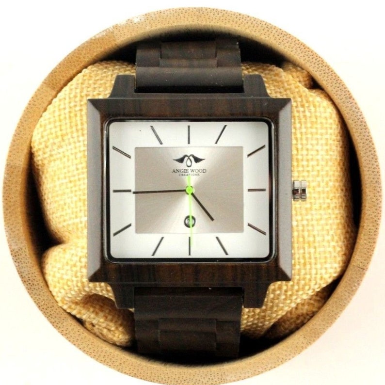 May include: A square-shaped wooden wristwatch with a brown wood band and a white face. The watch face has black hour and minute hands, a green second hand, and the text "Angie Wood Creations" printed on it.