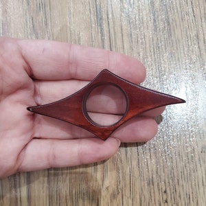 May include: A dark red wooden bookmark shaped like a diamond with a circular hole in the center.