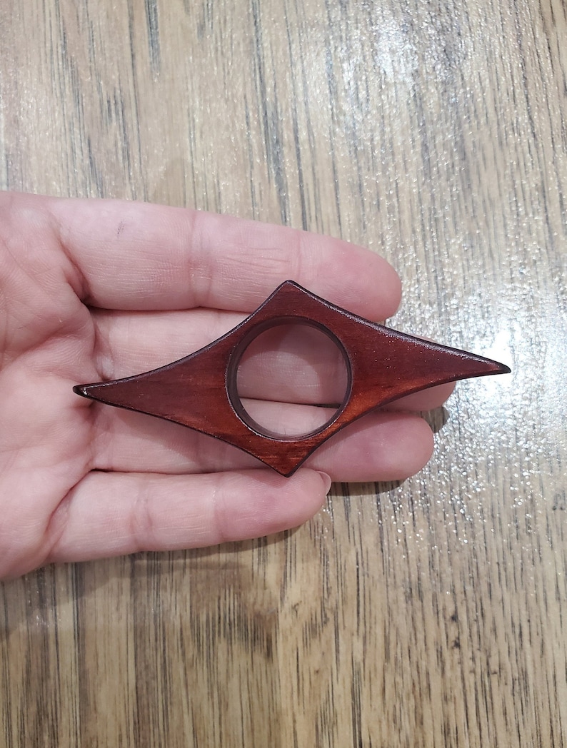 May include: A dark red wooden bookmark shaped like a diamond with a circular hole in the center.
