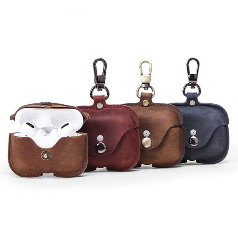 May include: Three leather cases for wireless earbuds with a carabiner clip. The cases are brown, red, and blue.