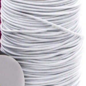May include: A spool of white elastic cord. The cord is tightly wound around a white cardboard core. A partial view of a pink spool is visible in the background. The elastic cord is used for sewing and crafting projects.