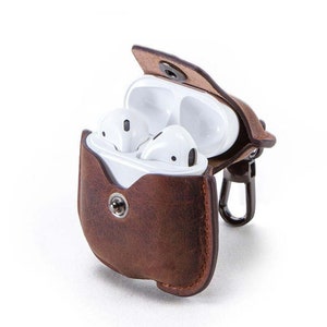 May include: A brown leather case with a snap closure for AirPods. The case has a metal carabiner attached to it.
