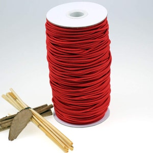 May include: A spool of bright red elastic cord wound around a white cardboard tube. The cord is smooth and appears to be made of a stretchy material.