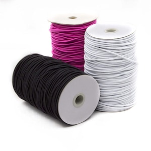 May include: Three spools of elastic cord in black, fuchsia, and white. The elastic is tightly wound on white cardboard spools. The cords are suitable for various crafting and sewing projects.