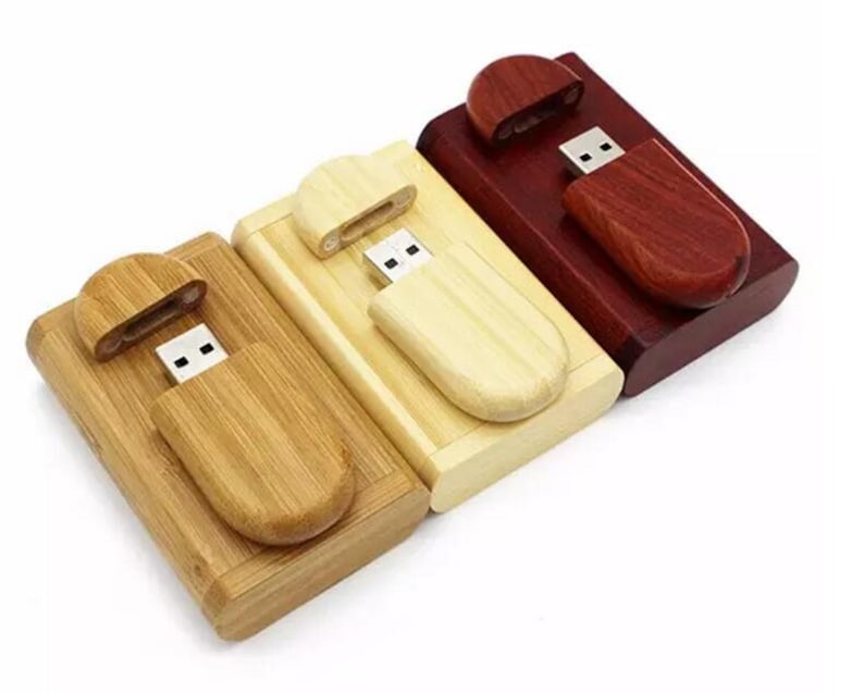 K&ouml;nnte beinhalten: Drei USB-Sticks aus Holz in verschiedenen Farben: Naturholz, helles Holz und dunkelrot. Jeder Stick hat eine Schiebekappe, die den USB-Anschluss freigibt.