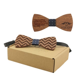 Puede incluir: Una pajarita de madera con un patrón de chevron y una banda con estampado azul y blanco. La pajarita está en una caja de cartón marrón. La pajarita está grabada con el texto "I keep myself busy with the things I do, But every time I pause, I still think of you Love J&M" y "Angie Wood Creations".
