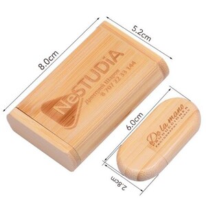 K&ouml;nnte beinhalten: Eine Holzkiste mit Deckel, die 8 cm x 6 cm x 5,2 cm misst, mit dem Text "NESTUDIA" und Kontaktinformationen, die auf der Oberseite eingraviert sind. Die Kiste ist ge&ouml;ffnet und eine kleinere Holzkiste mit dem Text "De la mano" befindet sich im Inneren. Die kleinere Kiste misst 2,8 cm x 6 cm.