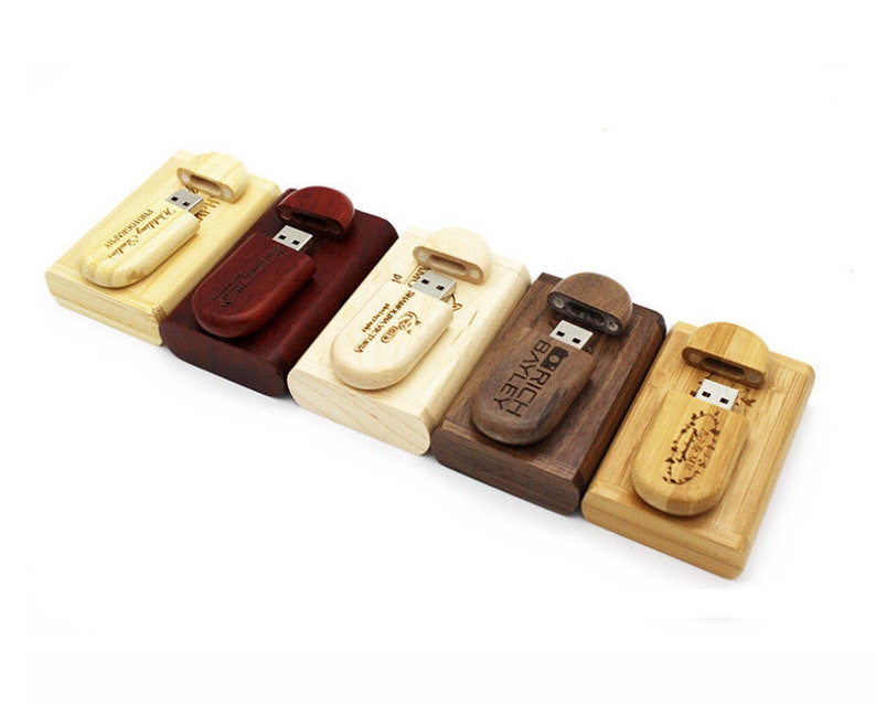 K&ouml;nnte beinhalten: F&uuml;nf USB-Sticks aus Holz mit personalisierten Gravuren. Jeder Stick ist aus einer anderen Holzart und hat eine Schiebekappe, um den USB-Anschluss freizulegen.