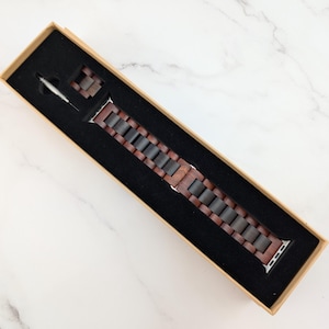 May include: A brown wooden watch band with a silver buckle in a brown box.