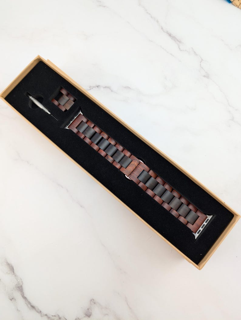 May include: A brown wooden watch band with a silver buckle in a brown box.