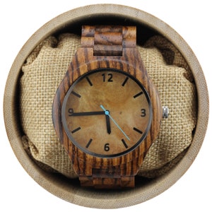 May include: A wooden wristwatch with a brown wood band and a brown face with black markings. The watch is in a brown box with a burlap lining.