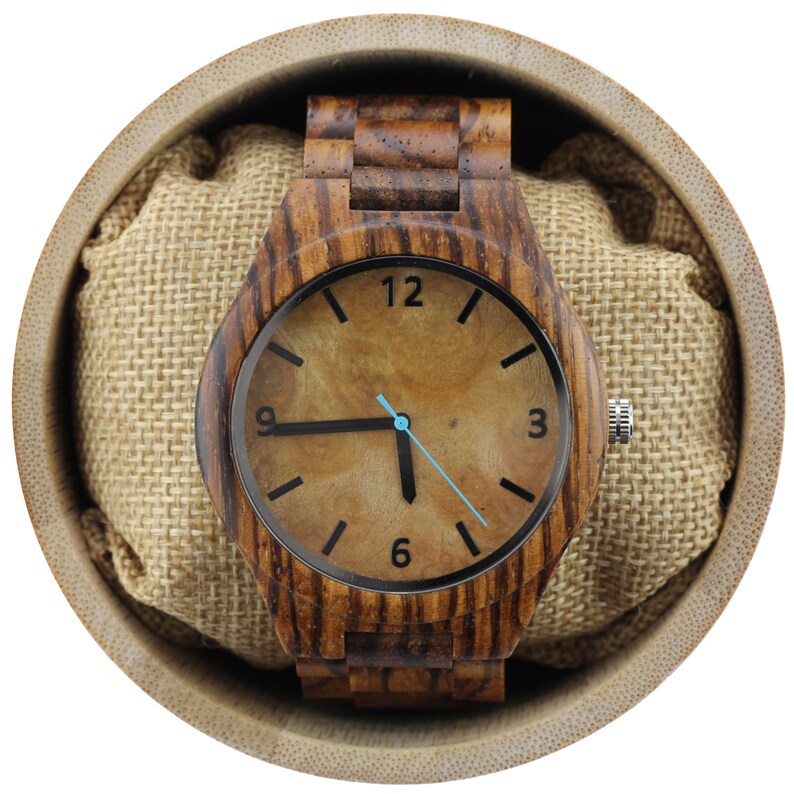 May include: A wooden wristwatch with a brown wood band and a brown face with black markings. The watch is in a brown box with a burlap lining.
