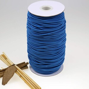 May include: A spool of bright blue elastic cord wound around a white cardboard core. The elastic cord is used for crafts, sewing, and jewelry making.