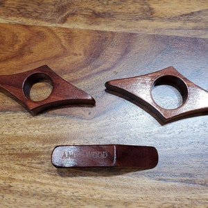 May include: Three wooden bookends in the shape of a diamond with a rounded hole in the center. The bookends are a dark reddish brown color. The bottom bookend has the words "AMERICAN WOOD" engraved on it.