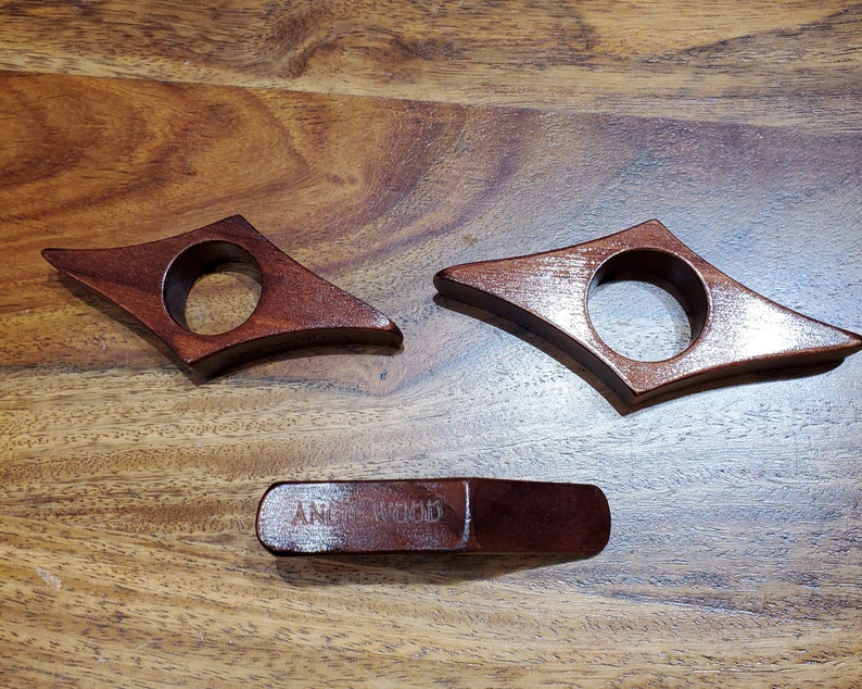 May include: Three wooden bookends in the shape of a diamond with a rounded hole in the center. The bookends are a dark reddish brown color. The bottom bookend has the words "AMERICAN WOOD" engraved on it.