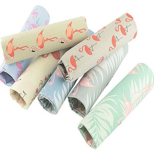 May include: A set of eight fabric scraps featuring a flamingo pattern in various colors, including green, blue, and beige. The fabric scraps are rolled up and arranged in a pile.