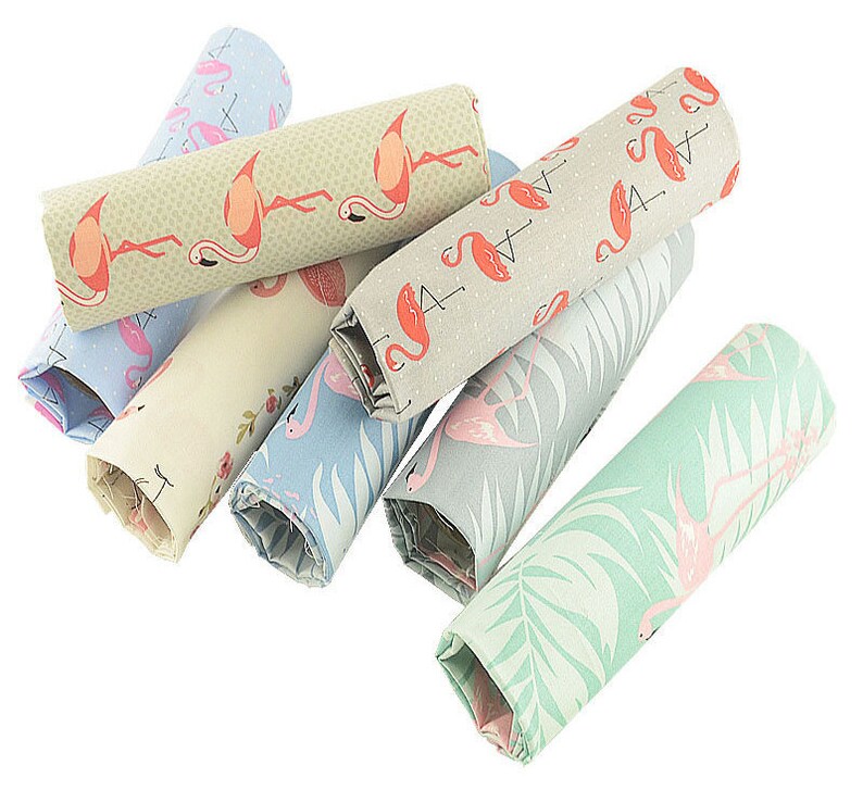 May include: A set of eight fabric scraps featuring a flamingo pattern in various colors, including green, blue, and beige. The fabric scraps are rolled up and arranged in a pile.