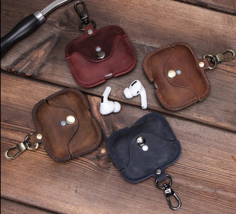 May include: Four leather cases for wireless earbuds with a metal keychain. The cases are in brown, dark brown, red, and black.