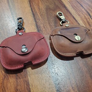 May include: Two leather Airpod cases with a metal clasp. One case is red and the other is brown.