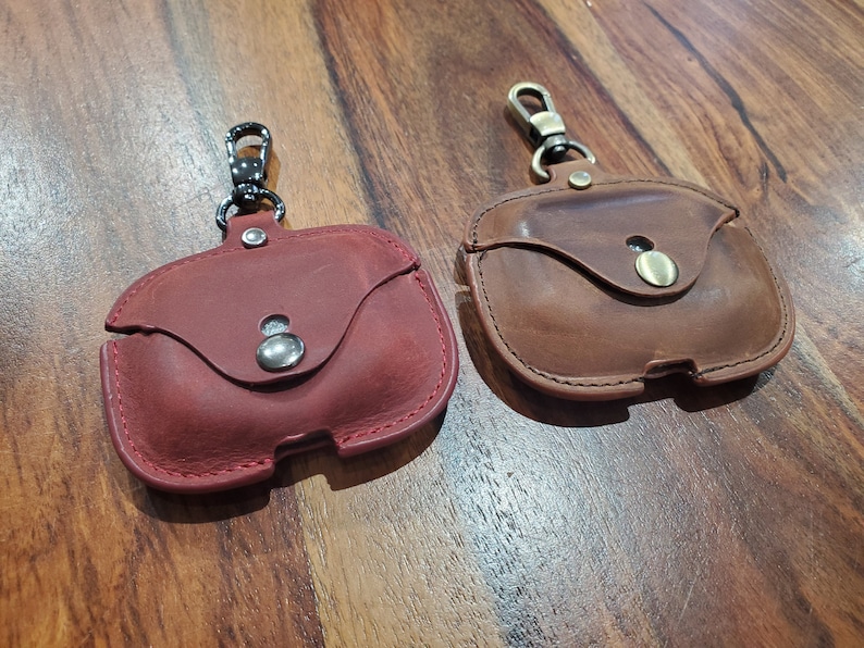 May include: Two leather Airpod cases with a metal clasp. One case is red and the other is brown.