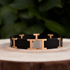 May include: A black and gold bracelet with a stainless steel clasp. The bracelet is made of a black material that looks like wood.