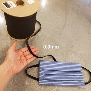 May include: A spool of black elastic cord with a label that reads "0.9mm" and a blue and white striped fabric face mask with black elastic straps.