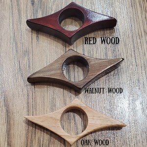 May include: Three wooden bookends in the shape of a diamond with a rounded center hole. The bookends are made of red wood, walnut wood, and oak wood. The text "RED WOOD", "WALNUT WOOD", and "OAK WOOD" is printed below each bookend.
