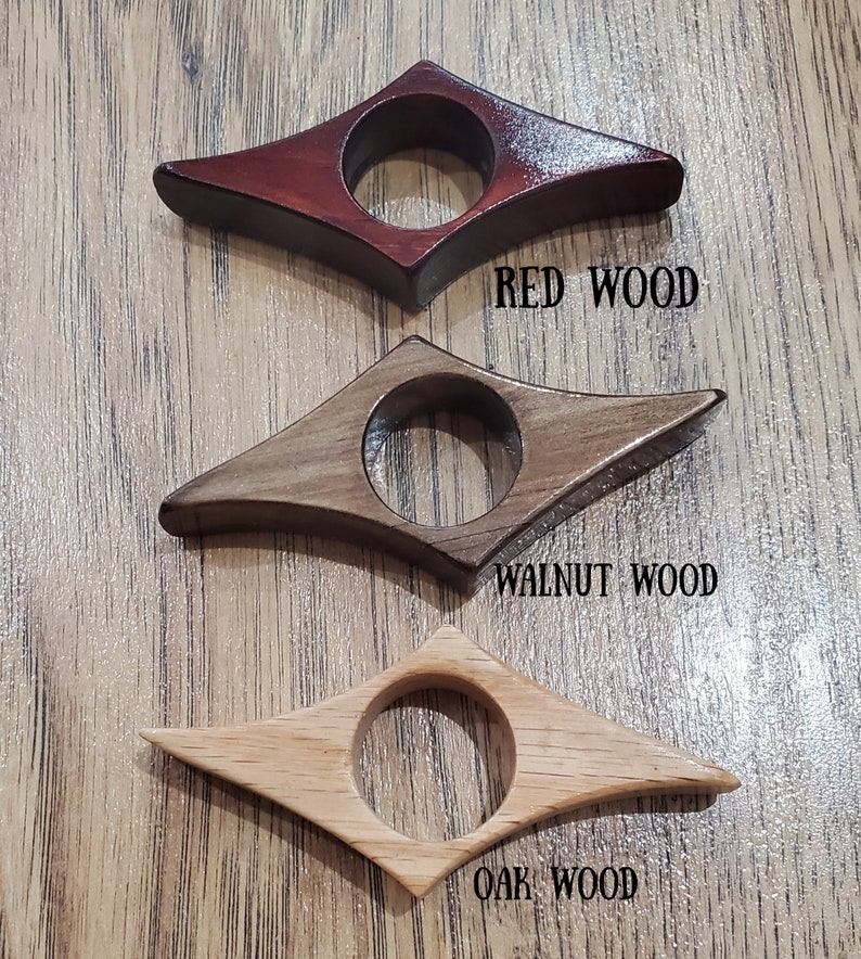 May include: Three wooden bookends in the shape of a diamond with a rounded center hole. The bookends are made of red wood, walnut wood, and oak wood. The text "RED WOOD", "WALNUT WOOD", and "OAK WOOD" is printed below each bookend.