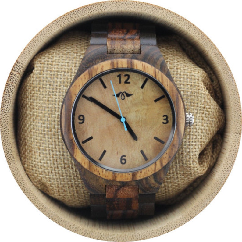 May include: A wooden wristwatch with a brown and black wood band and a light brown face with black markings. The watch is in a bamboo box with a brown fabric lining.