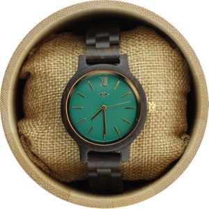 May include: A wooden wristwatch with a green face and gold hands. The watch is in a bamboo box with a brown fabric lining.