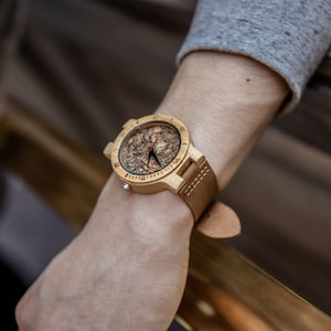 May include: A wooden wristwatch with a brown leather strap. The watch face is made of wood and has a unique pattern. The watch hands are black.