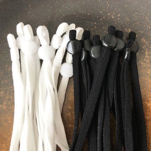 May include: A set of white and black elastic mask strap extenders with adjustable toggles. The extenders are made of a soft, stretchy material and have a comfortable fit.