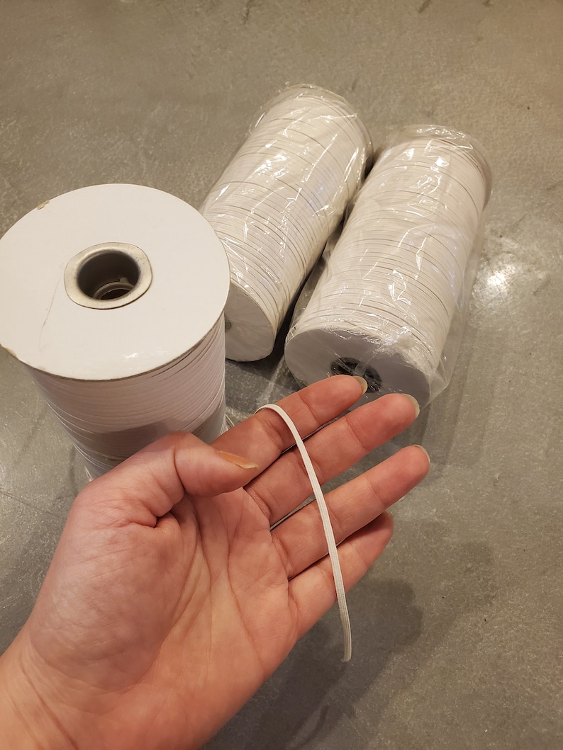 May include: Three spools of white elastic cord, wrapped in clear plastic, with one piece of elastic cord in a hand.