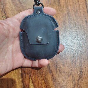 May include: A dark blue leather case with a metal clasp and a loop for attaching to a keychain. The case has a small pocket on the front.
