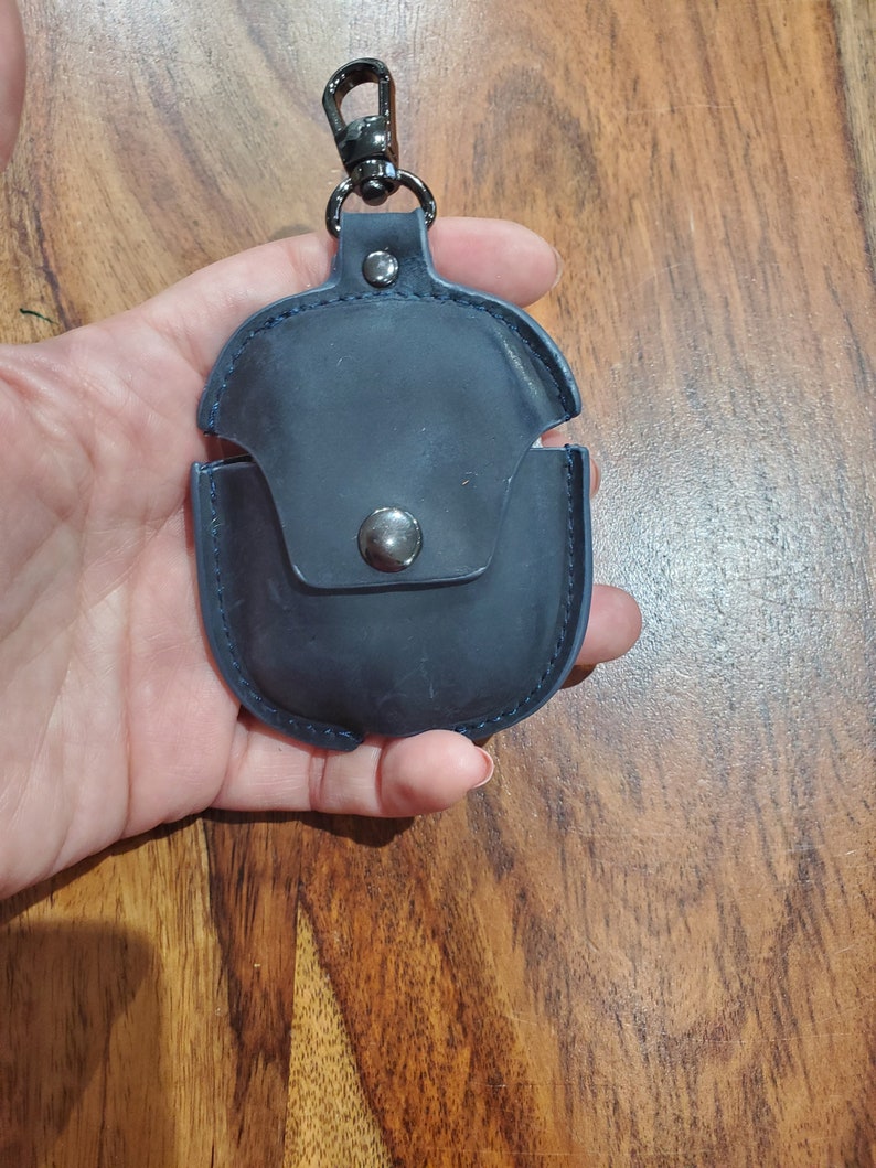 May include: A dark blue leather case with a metal clasp and a loop for attaching to a keychain. The case has a small pocket on the front.