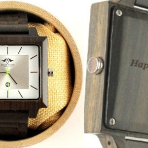 May include: A square wooden watch with a silver face and black hands. The watch is in a box with a brown fabric lining. The back of the watch has an engraved message that reads "Happy 5th Sean. Love, Katie."